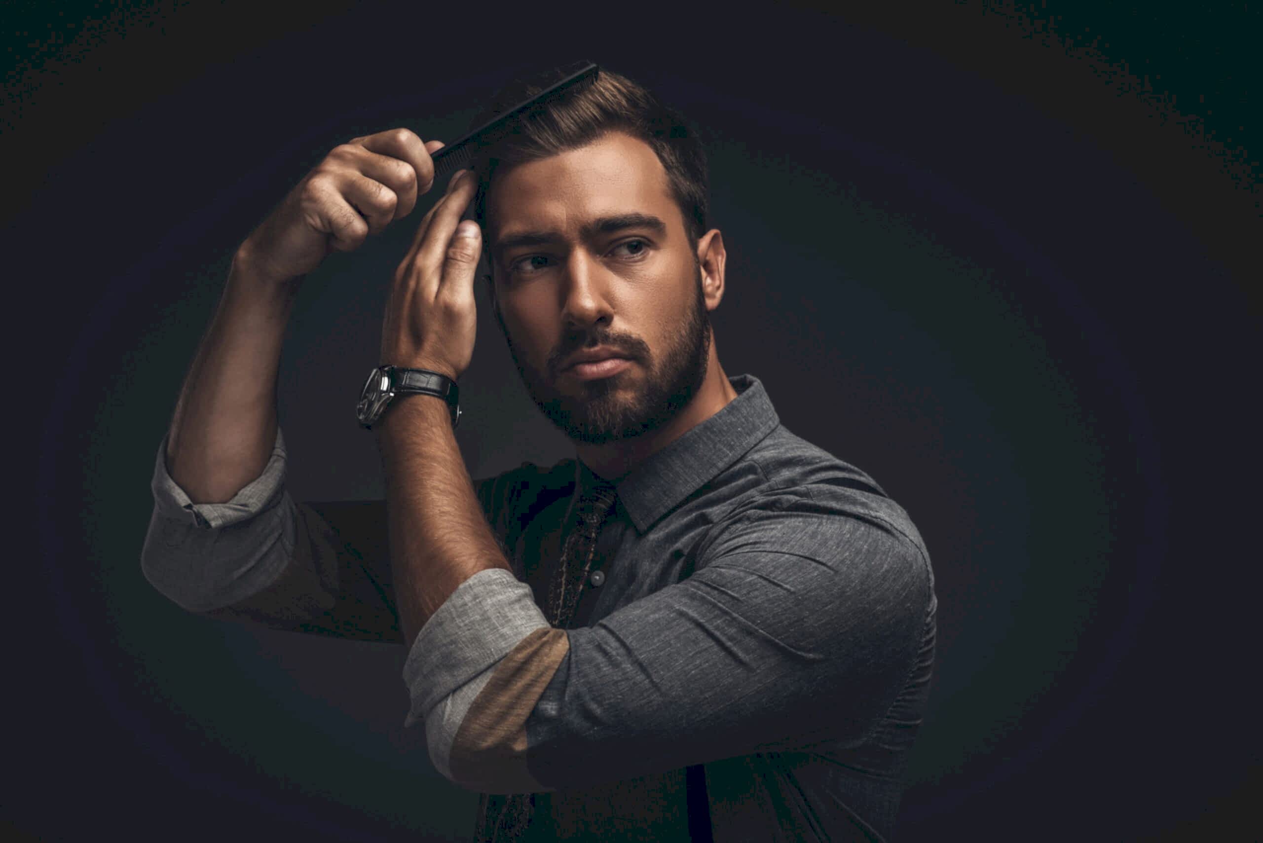 Handsome man styling his hair, black background